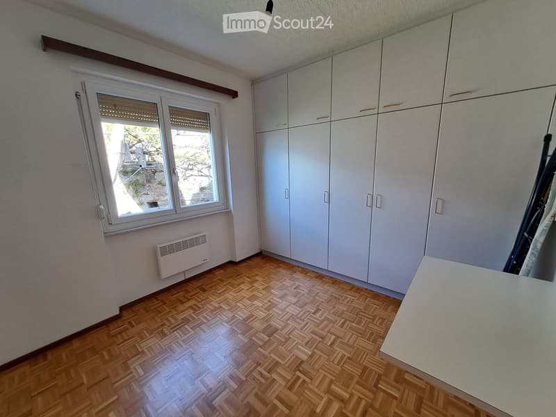 Empty room with wooden floor, white walls, large window, white cabinets, white desk, white radiator