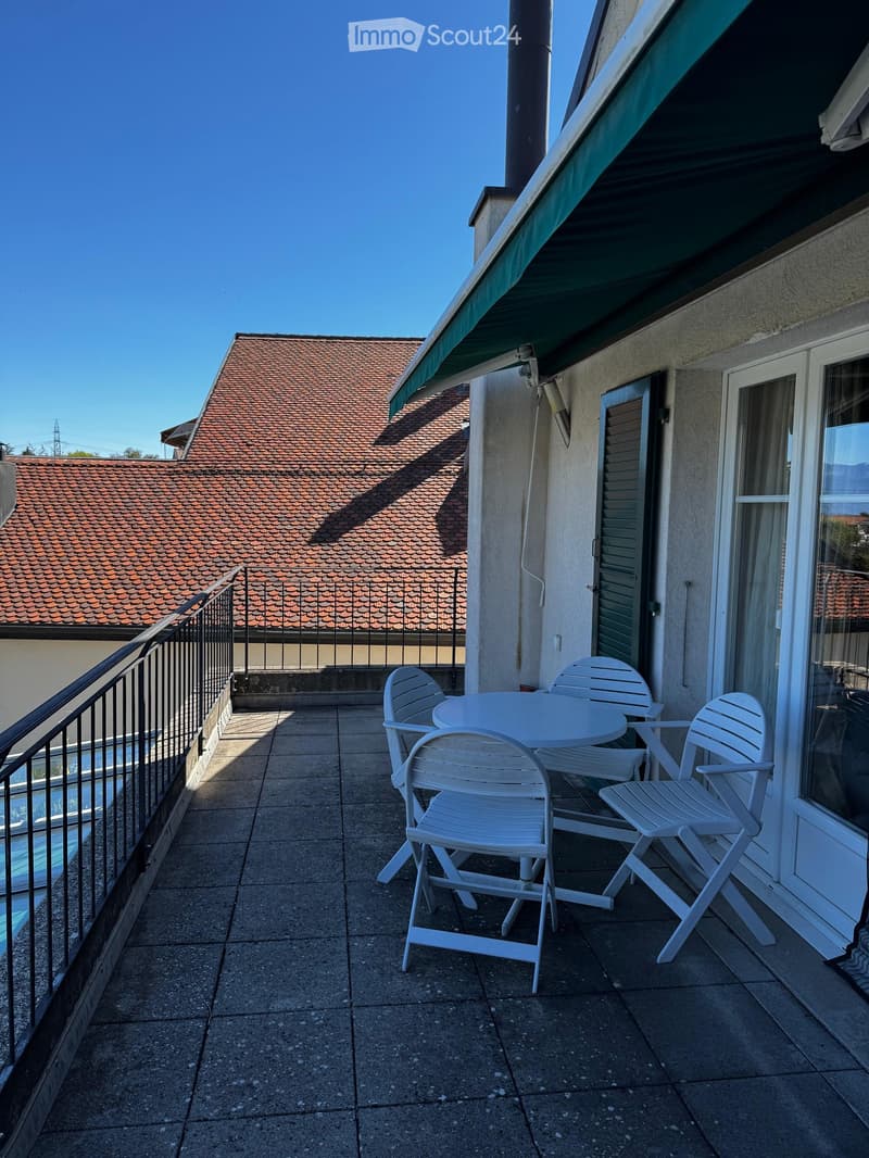 Balcony with a white table and four white chairs, overlooking neighboring rooftops.