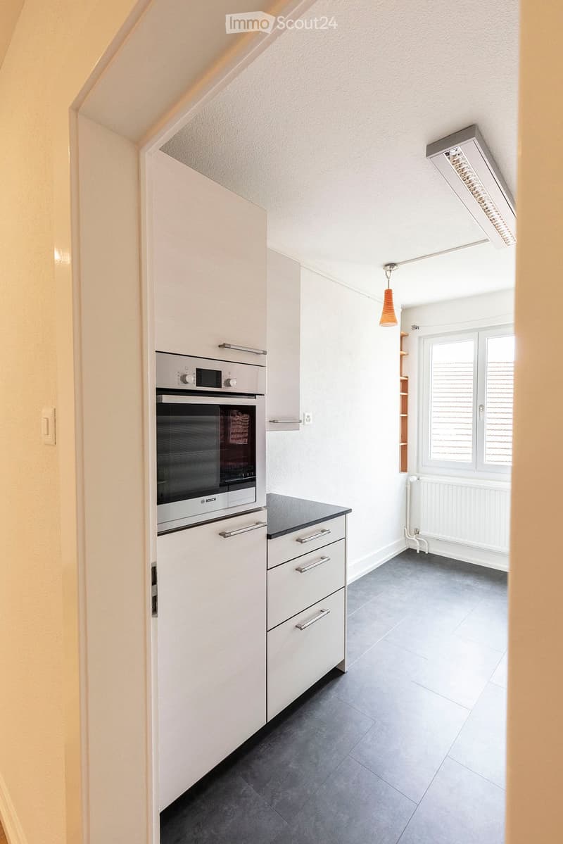 Modern kitchen with white cabinets, stainless steel oven, dark countertop, and grey tiled floor.