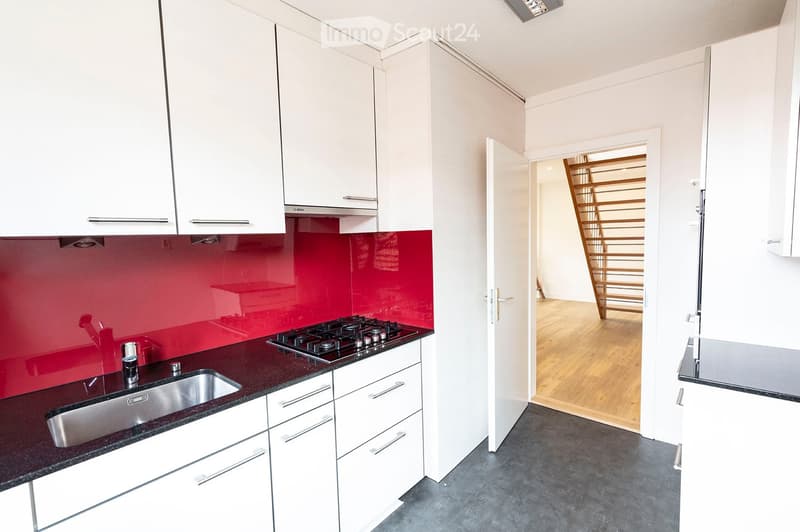 Modern kitchen with white cabinets, dark countertops, and a red backsplash. Features a stainless steel sink and a gas stove.