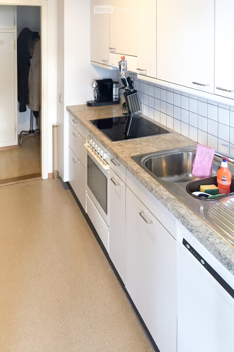 Modern kitchen with white cabinets, granite countertop, stainless steel sink, built-in oven, and coffee maker.