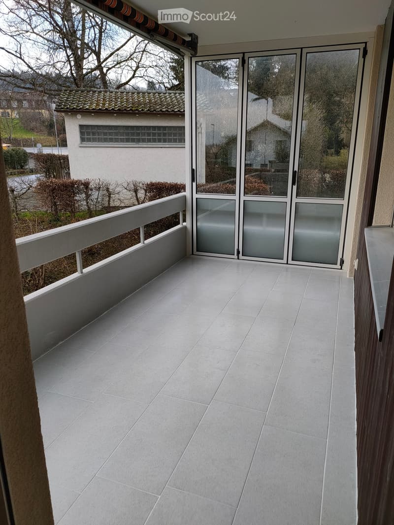 Balcony with tiled floor, glass sliding doors, white railing, and view of neighboring house and garden.