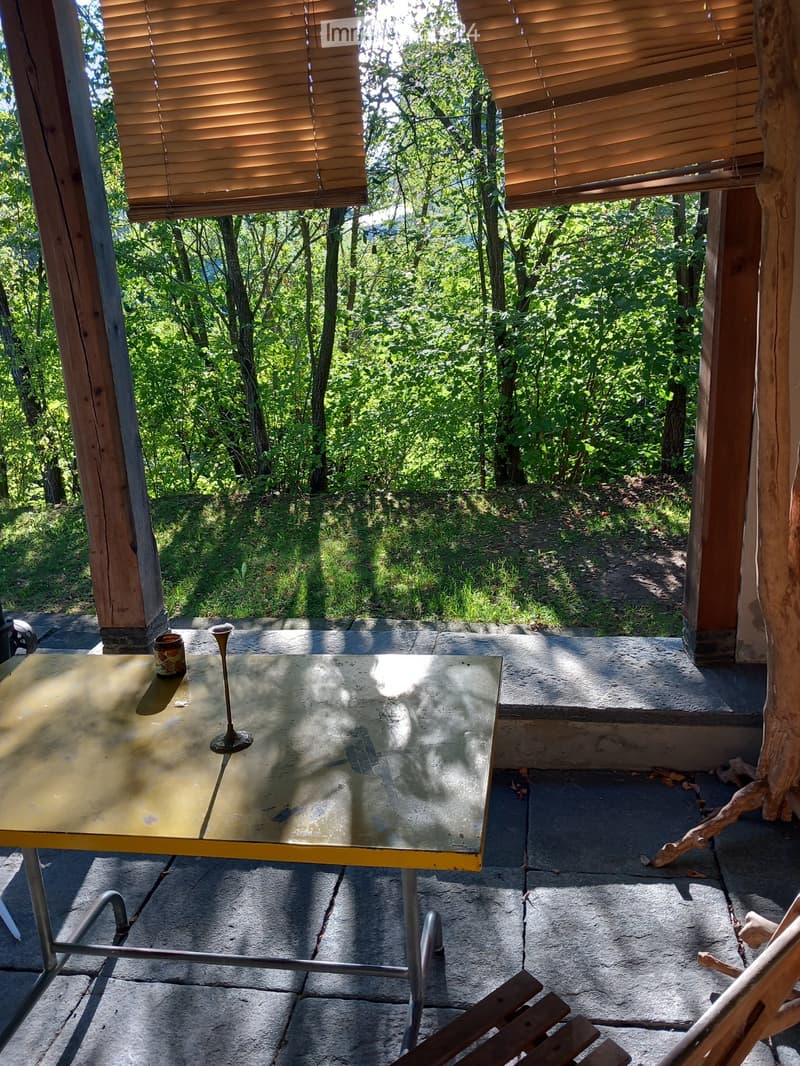 A wooden balcony with a metal table, a chair, and a small decorative item, overlooking a lush green forest.