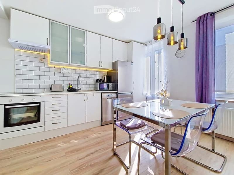 Modern kitchen with white cabinets, stainless steel appliances, a dining table with chairs, and pendant lights.