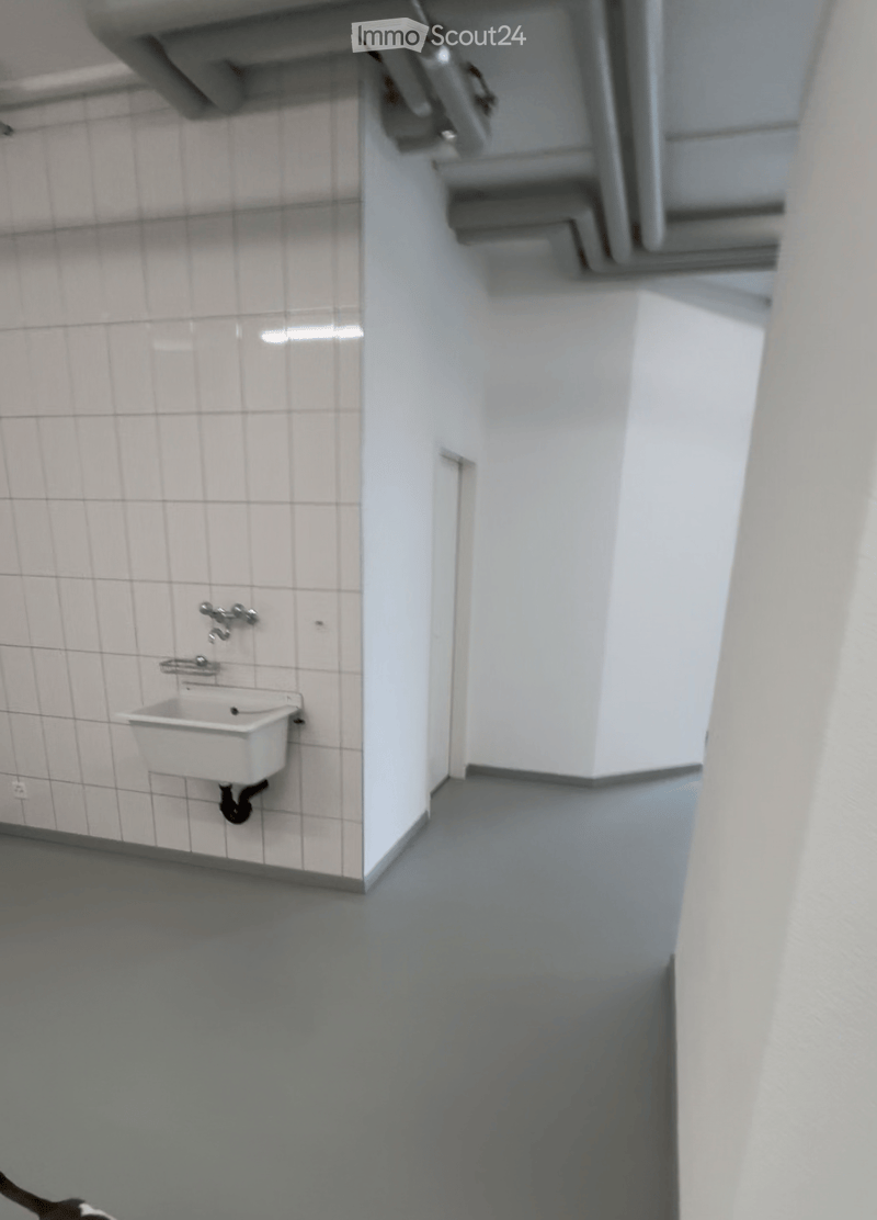 Bathroom with white tiled walls, a white sink, and a faucet. The floor is grey, and there is a staircase visible in the background.