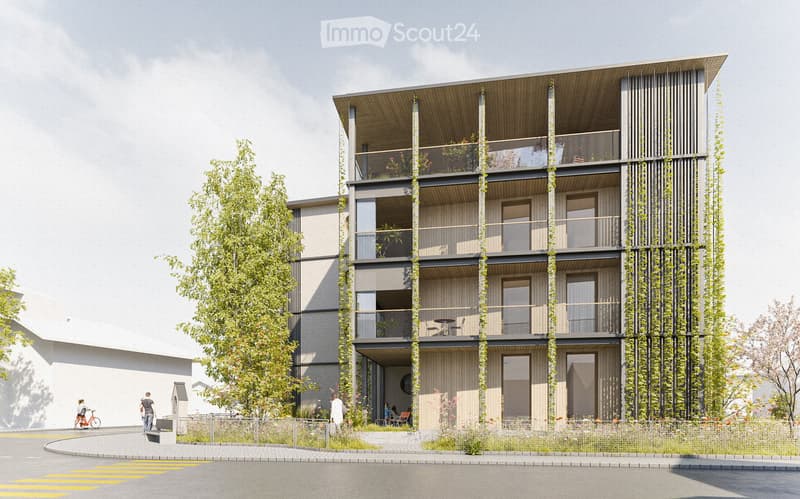Modern multi-story building with balconies, greenery, and contemporary design. Features include large windows, a raised ground floor, and a landscaped area in front.