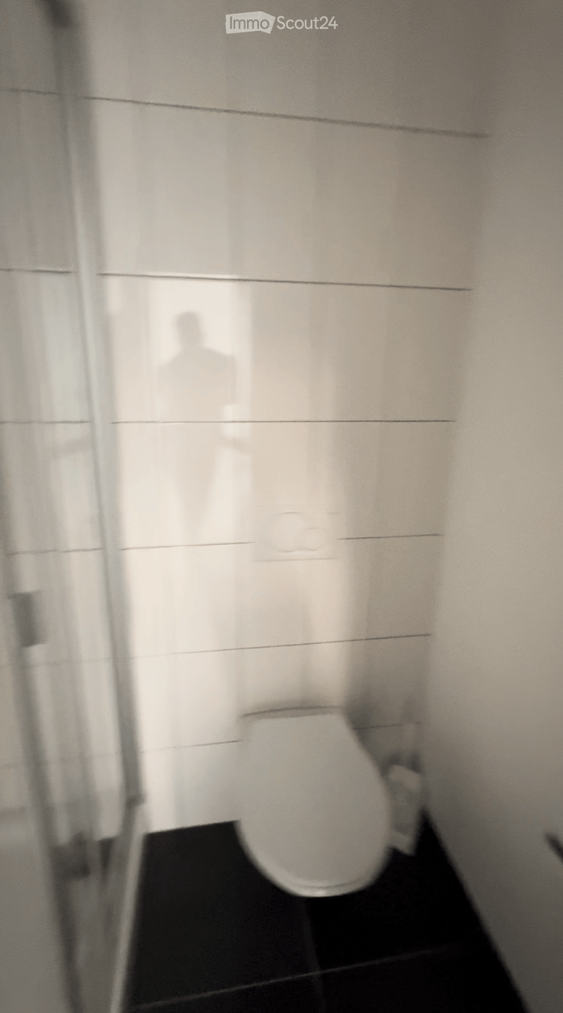Modern bathroom with white tiled walls and a toilet visible.