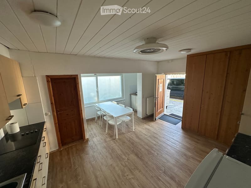 Open-plan kitchen and dining area with wooden flooring, white dining table and chairs, cabinets, and a sink.
