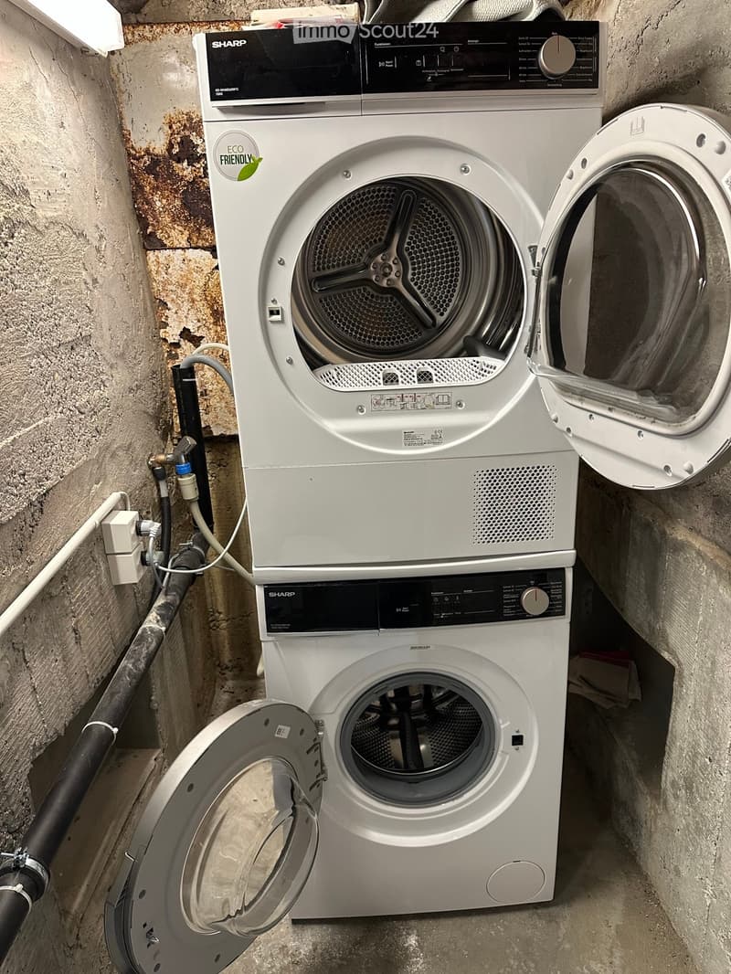 A small utility space with a washing machine and a dishwasher installed side by side, with exposed brick walls and visible plumbing.