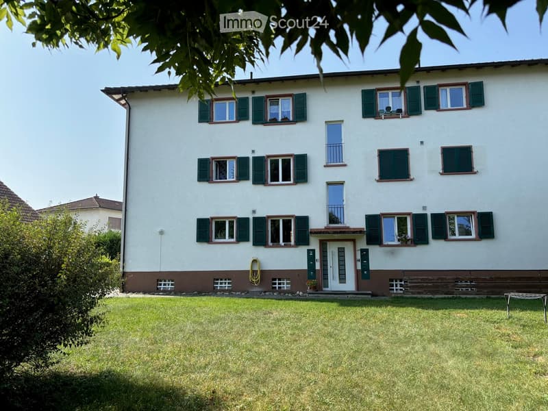Multi-unit apartment building with white exterior, green shutters, and a garden in the front.