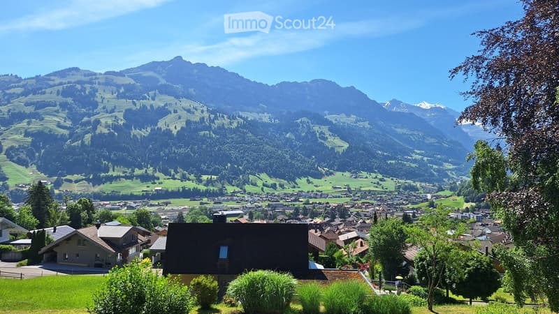 A scenic view of a town nestled in a valley surrounded by lush green hills and mountains, with a clear blue sky overhead.