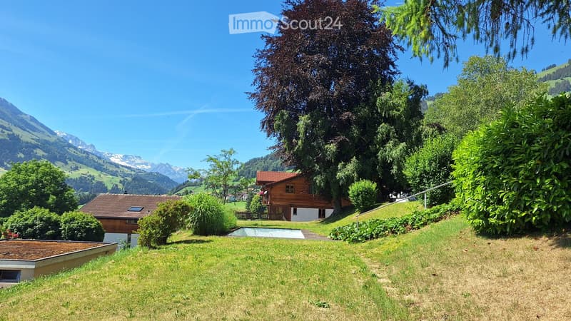 A serene garden area with two wooden houses, lush greenery, and a scenic mountain backdrop.