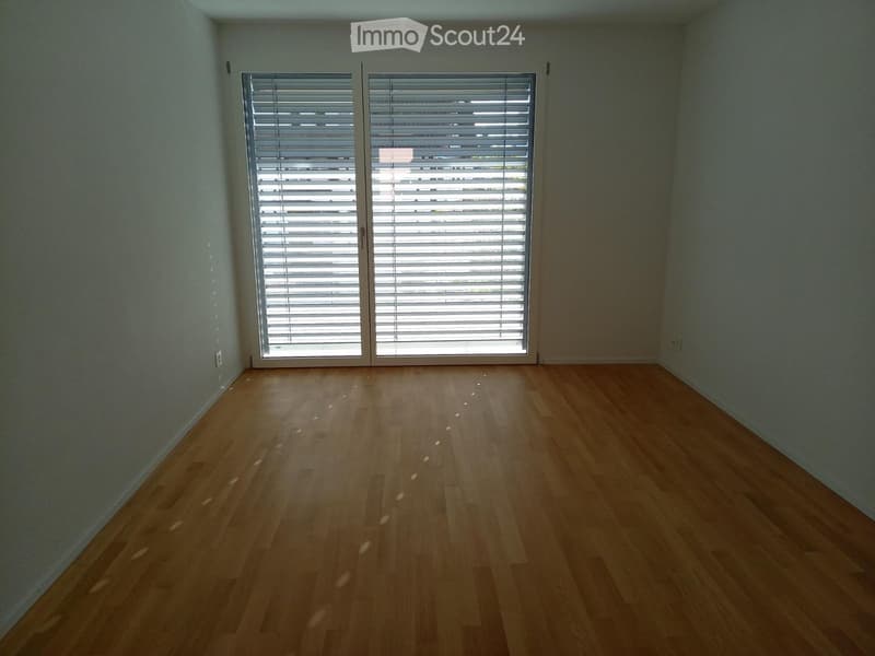 Empty room with light wooden flooring and large window with blinds, no furniture or equipment.