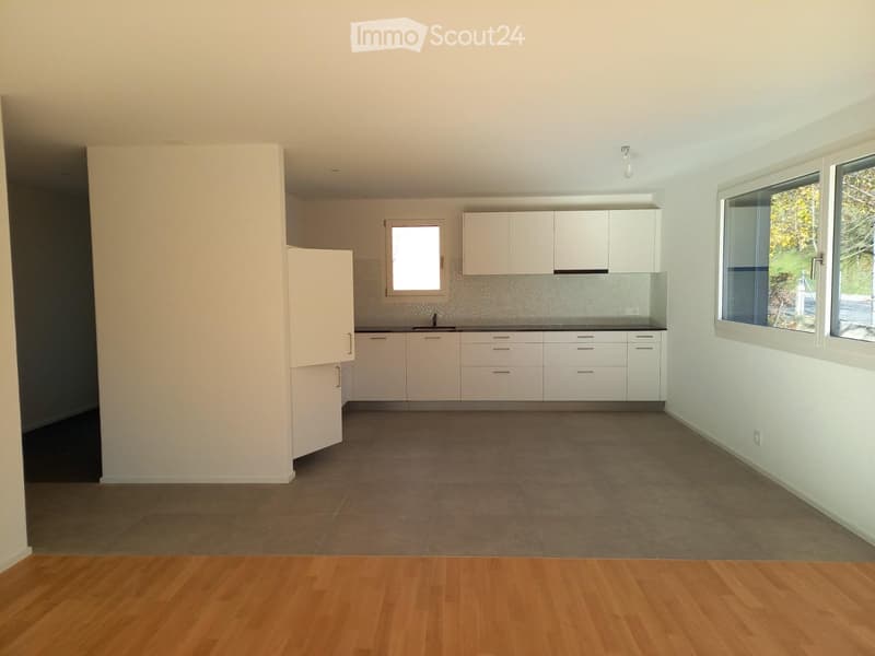Empty kitchen with white cabinets, tiled backsplash, and large windows. No appliances or furniture present.