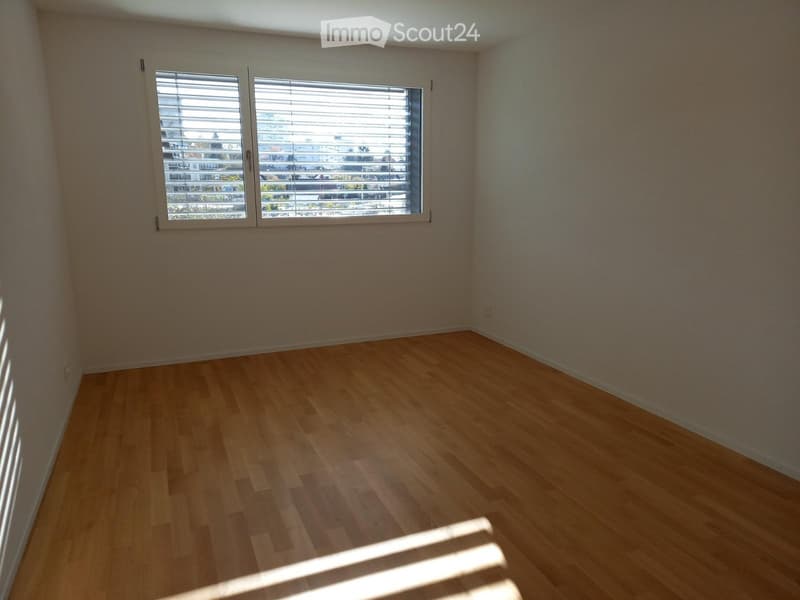 Empty room with wooden flooring, white walls, and large windows with blinds. No furniture or equipment present.