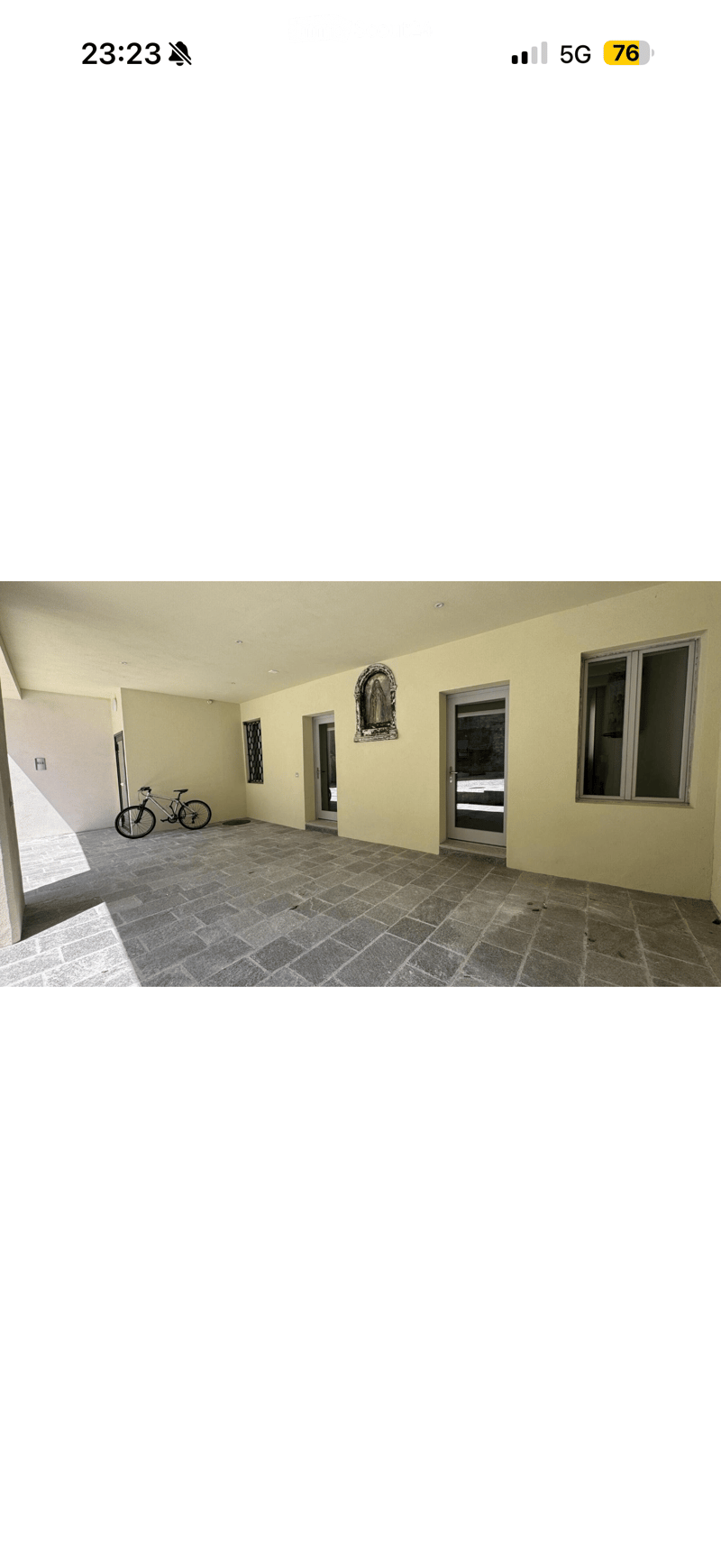 Empty outdoor patio area with tiled flooring, light yellow walls, and several doors leading to other spaces. A bicycle is parked near the left wall.