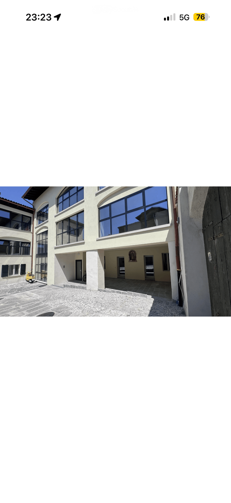 Modern multi-story building with large windows, a covered entrance area, and a paved courtyard.