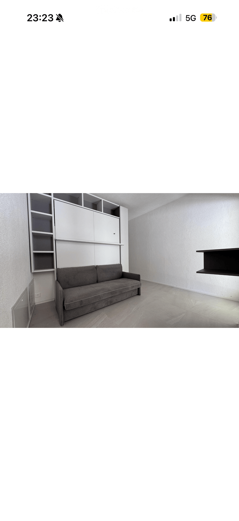 Modern living room with a grey sofa, built-in white shelves, and a sleek black floating shelf on the right side.