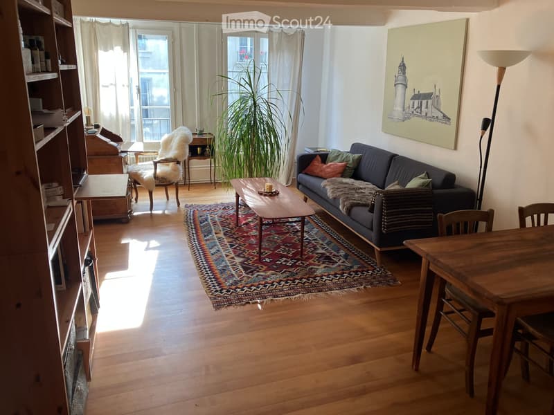 wooden floor, cozy couch, wooden coffee table, rug, armchair, wooden table, bookshelves, desk, painting, lamp, windows, curtains