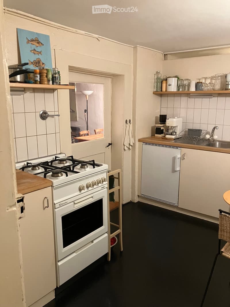 kitchen with white cabinets, black countertops, tiled walls, gas stove, fridge, sink, wine glasses, coffee machine