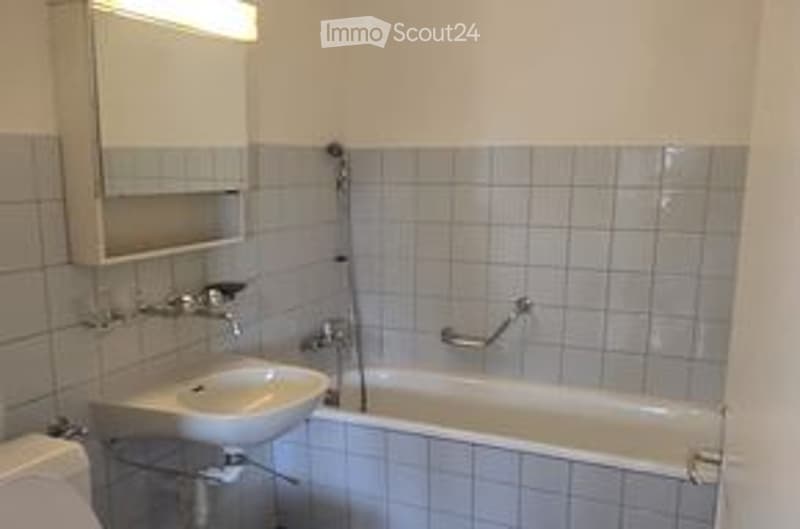 A small, clean bathroom with a white tiled wall, a sink, a bathtub, and a mirror above the sink.