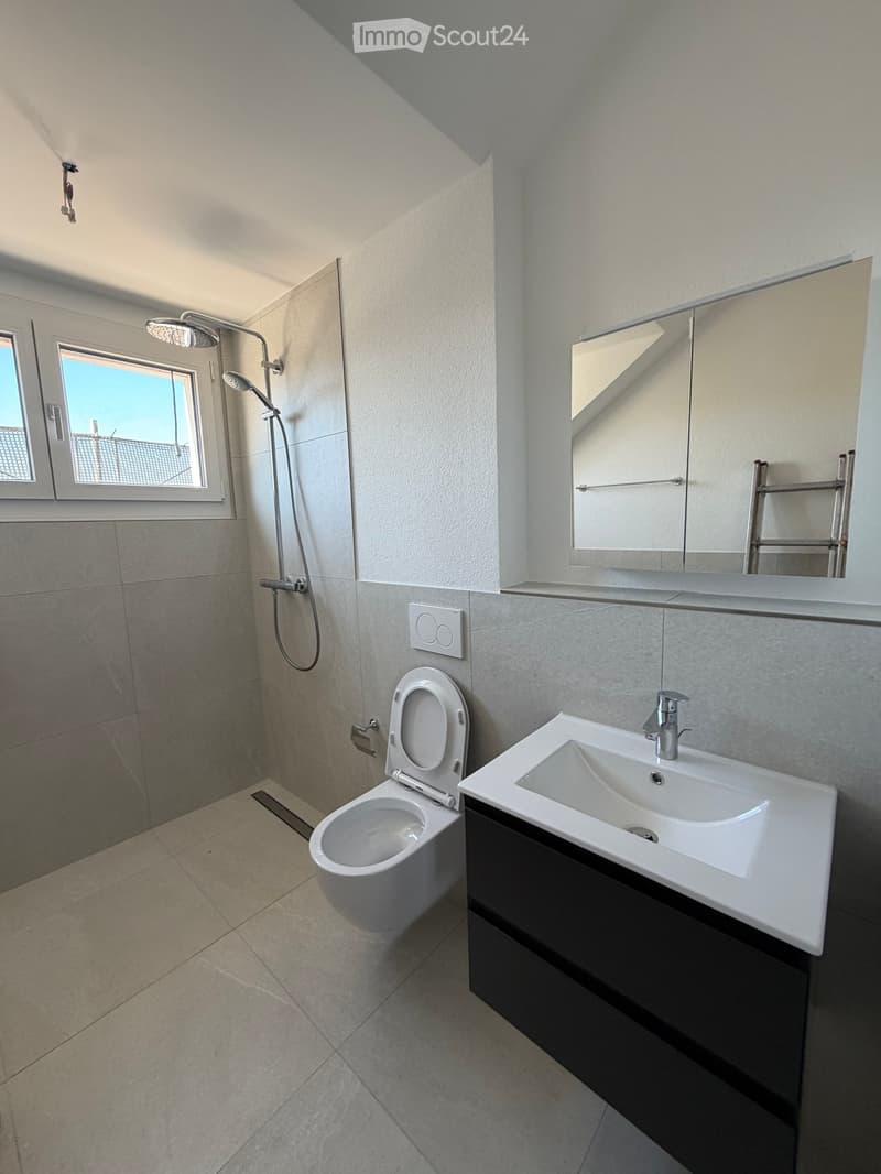 Modern bathroom with a toilet, sink, mirror, and shower. Features tiled walls and a window with a view.
