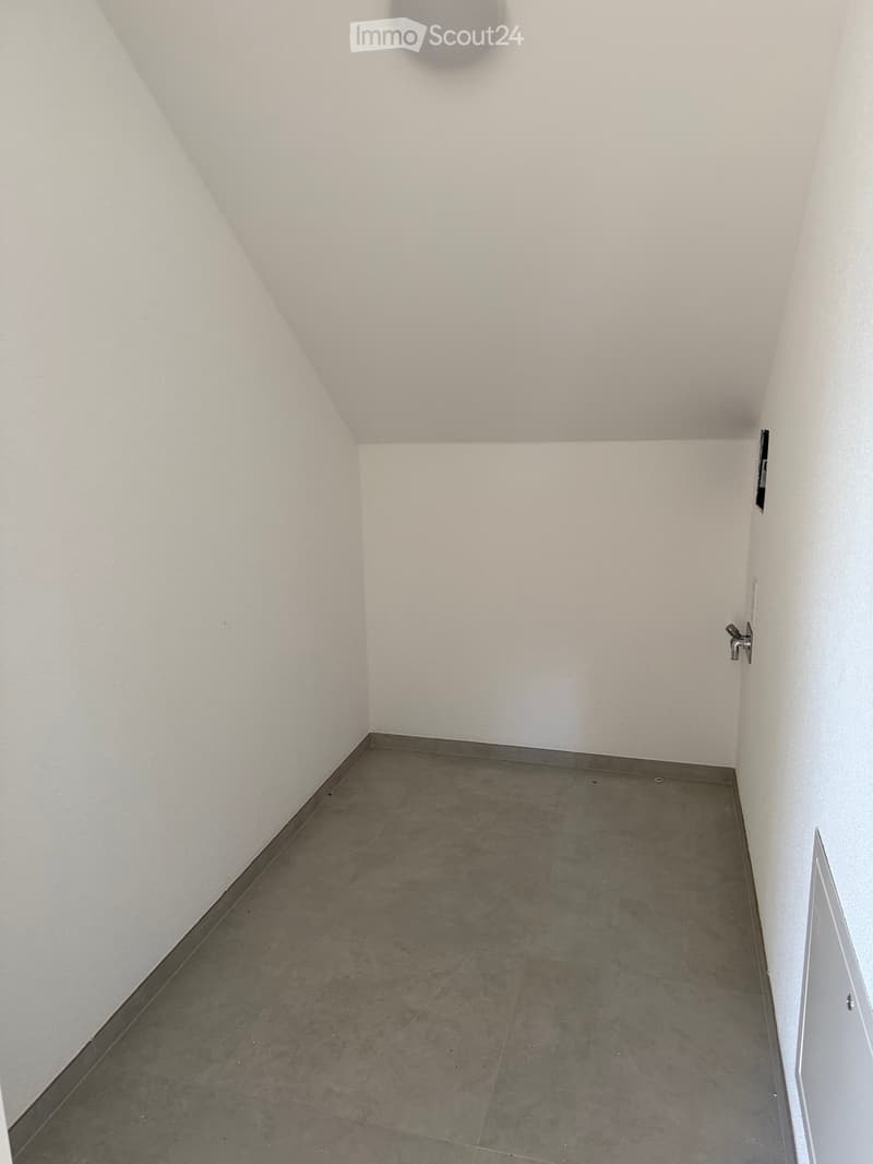 Empty room with white walls and grey tiled floor, no furniture or equipment visible.