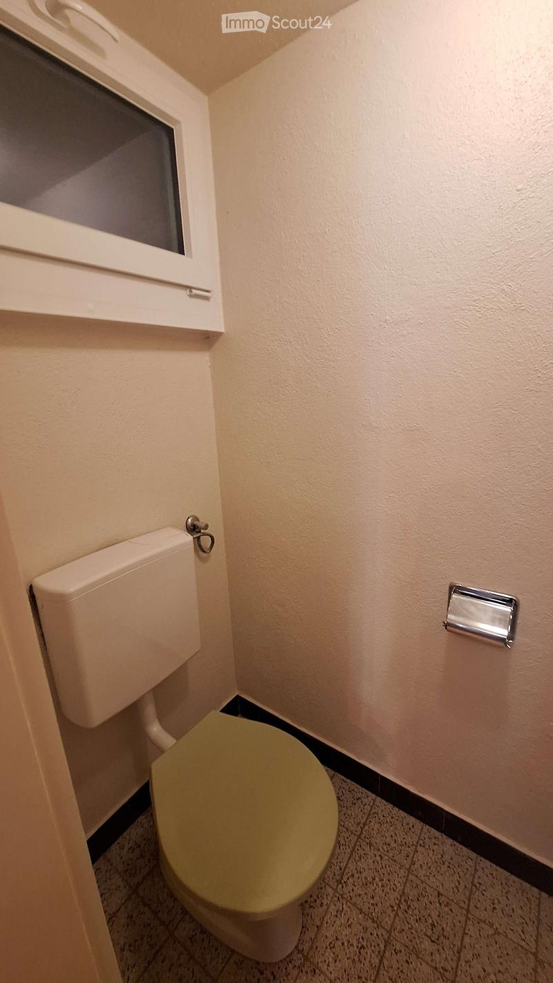 Small bathroom with a toilet, toilet paper holder, and a window above the toilet.
