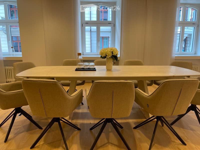 A modern dining area with a round table surrounded by chairs, a vase with flowers, and a bottle on the table.