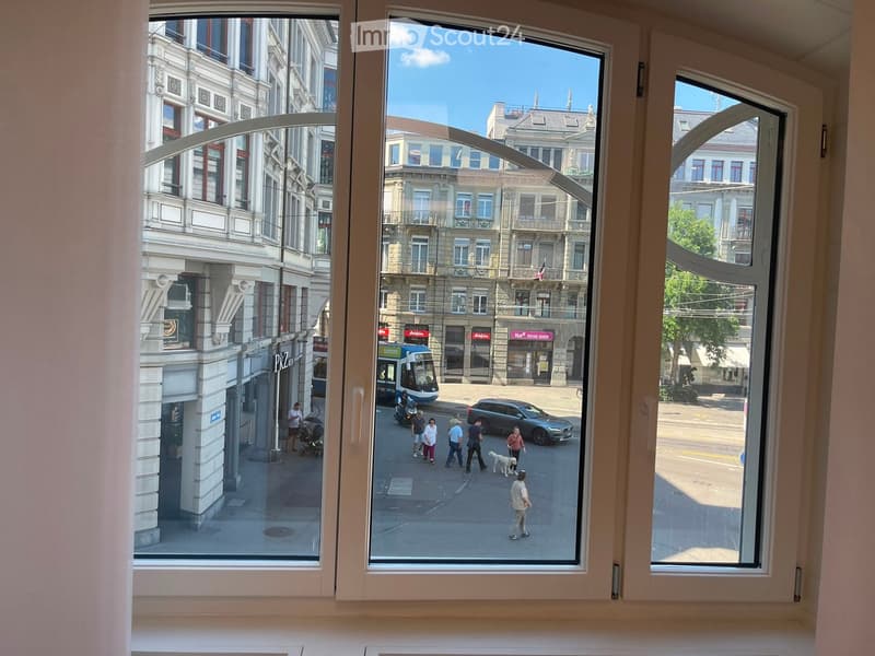 View from a room with large windows showing a busy urban street scene with pedestrians, cars, and buildings.