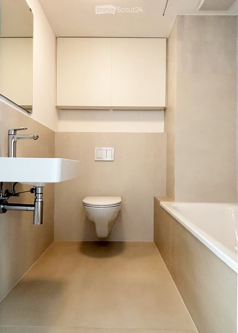 Modern bathroom with a white sink, chrome faucet, toilet, and bathtub, featuring light-colored tiles and a sleek design.