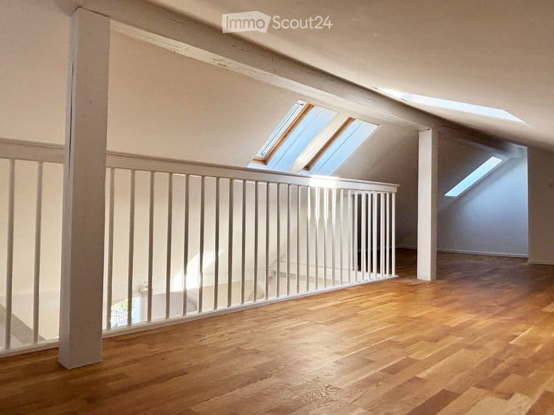 Empty room with wooden flooring, white railing, and skylight windows in the ceiling.