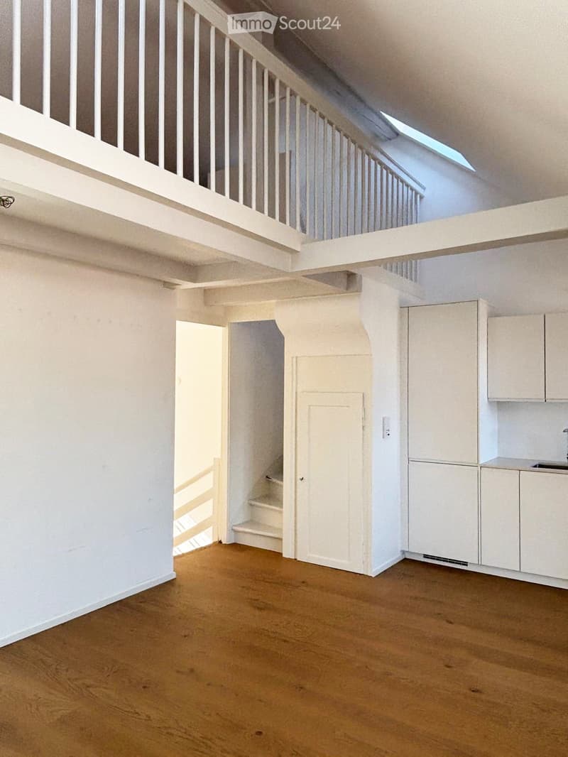 Empty room with wooden flooring, white walls, and a small built-in cabinet. A staircase leads to an upper level with a skylight.