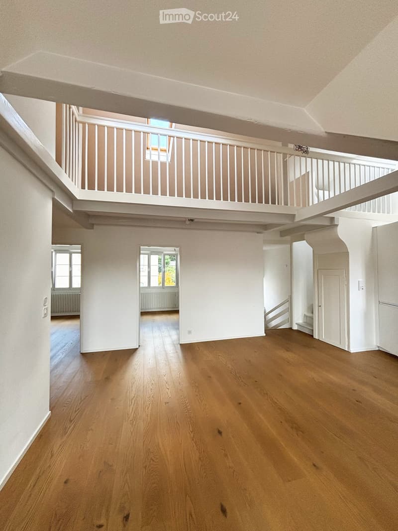 Empty room with wooden flooring, white walls, and a staircase leading to an upper level with a white railing and a window.