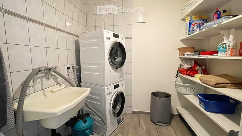 Bathroom with a stacked washer and dryer, a sink, shelves with cleaning supplies, and a towel hanging on the wall.