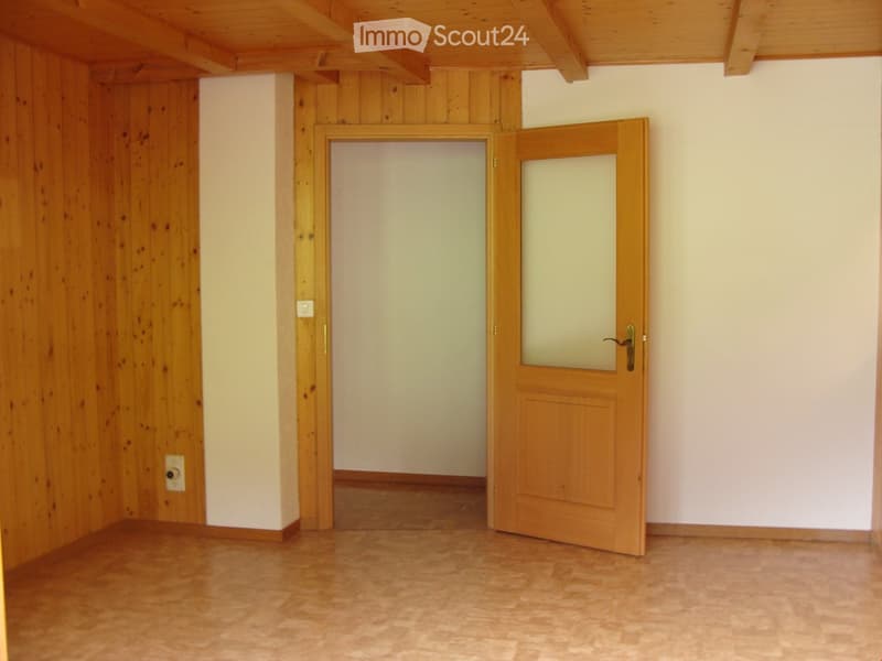 Empty room with wooden walls, wooden floor, and two wooden doors leading to another space.