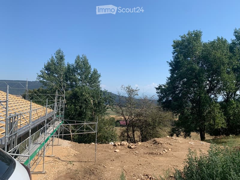 A building under construction with scaffolding, surrounded by trees and a clear blue sky.