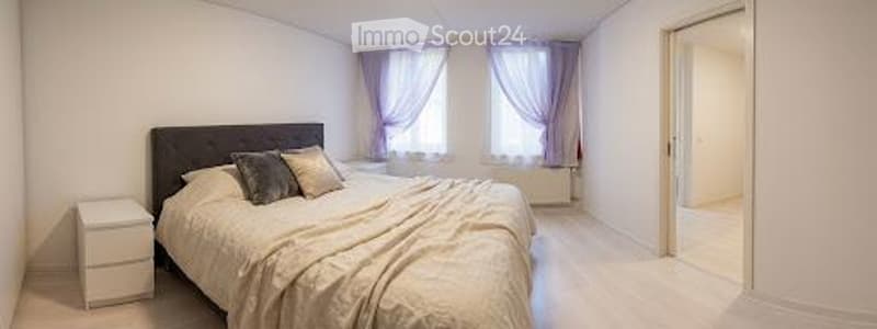 Bright bedroom with a large bed, nightstand, and two windows with curtains.