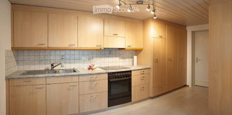 Modern kitchen with light wood cabinets, granite countertop, sink, oven, and track lighting.