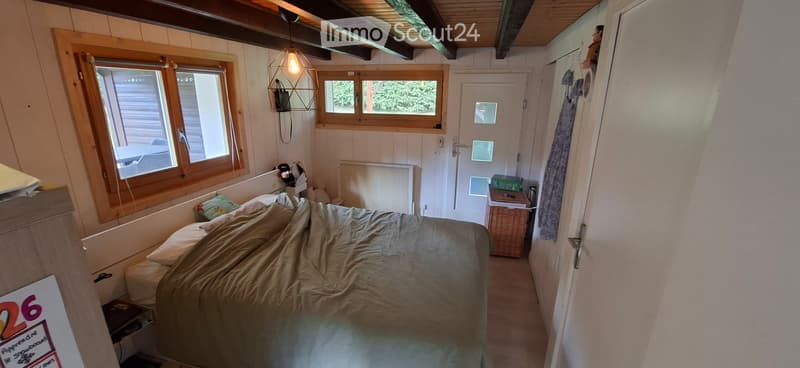 Cozy bedroom with a single bed, wooden walls, large windows, radiator, and a hanging light fixture.