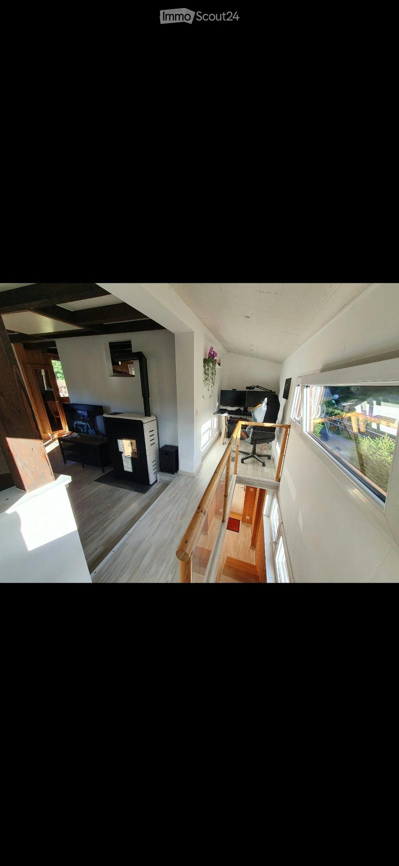 A modern, open-plan living and working space with a fireplace, desk, computer, and comfortable seating area.