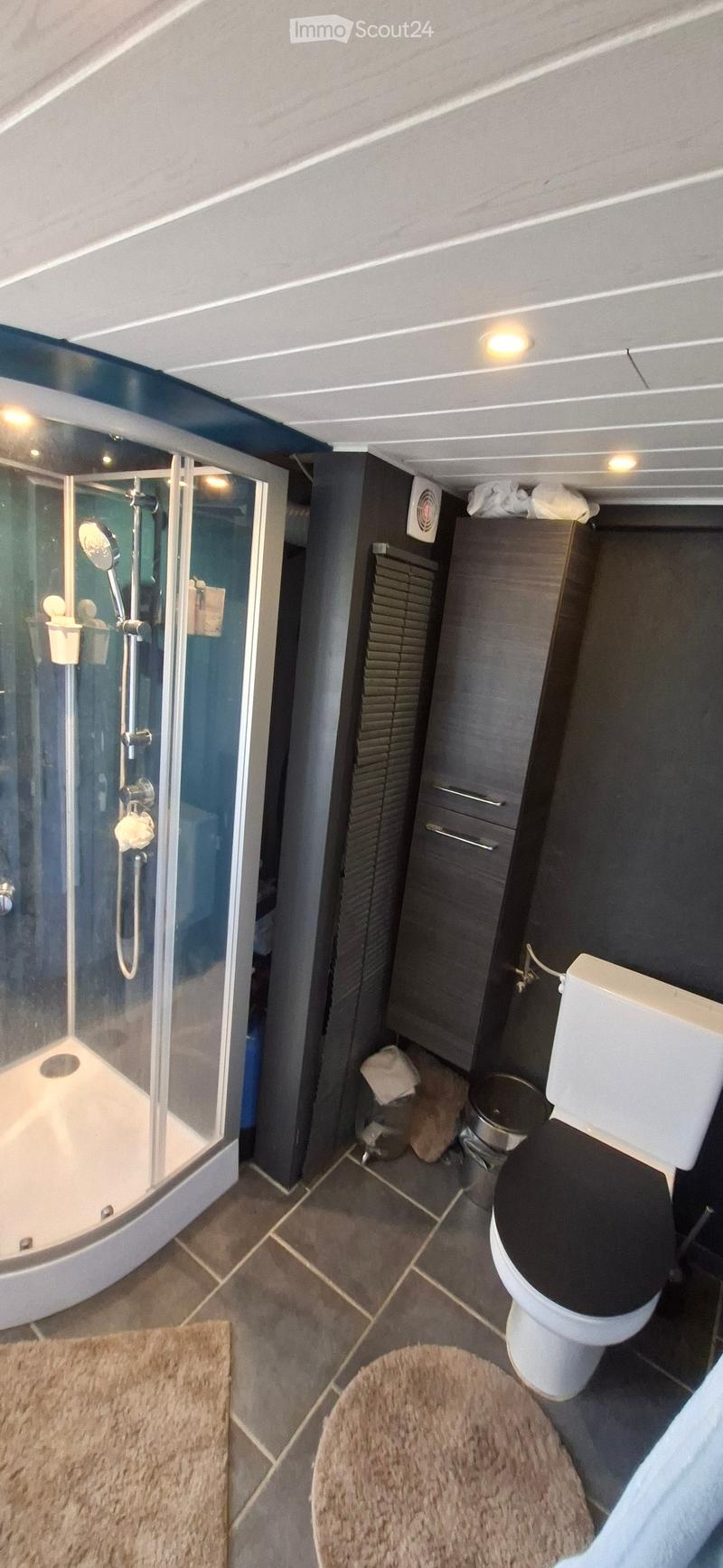 Modern bathroom with a shower stall, toilet, dark grey cabinet, and tiled floor.