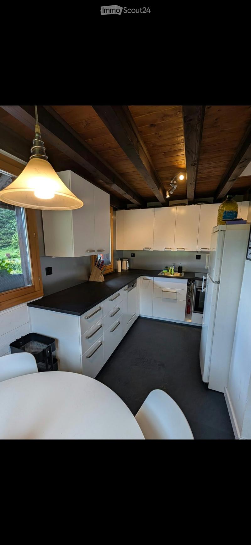 Modern kitchen with white cabinets, black countertop, stainless steel appliances, and a hanging light fixture. Features a dining area with a round table and stools.
