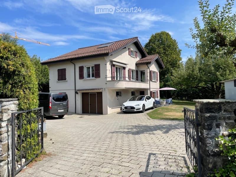 Two-story house with a tiled roof, multiple windows with shutters, a garage, and a driveway with two parked cars.