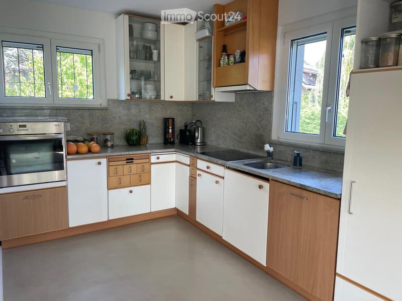 Modern kitchen with white and wooden cabinets, stainless steel appliances, granite countertops, and large windows letting in natural light.