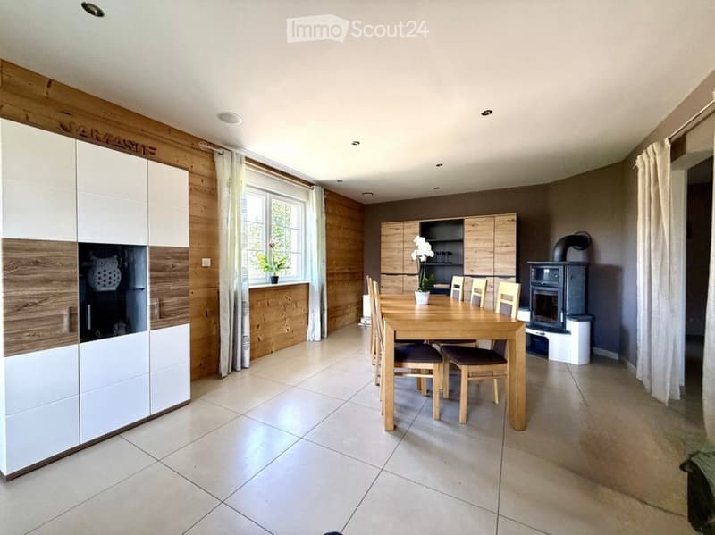 Modern dining area with a wooden dining table and chairs, kitchen cabinets, a fireplace, and a large window with curtains.