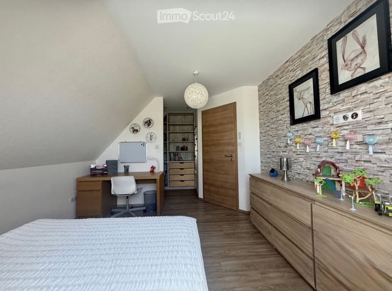 Cozy attic bedroom with slanted ceilings, wooden flooring, a bed, a desk with a chair, a bookshelf, a dresser with decorative items, and framed pictures on the wall.