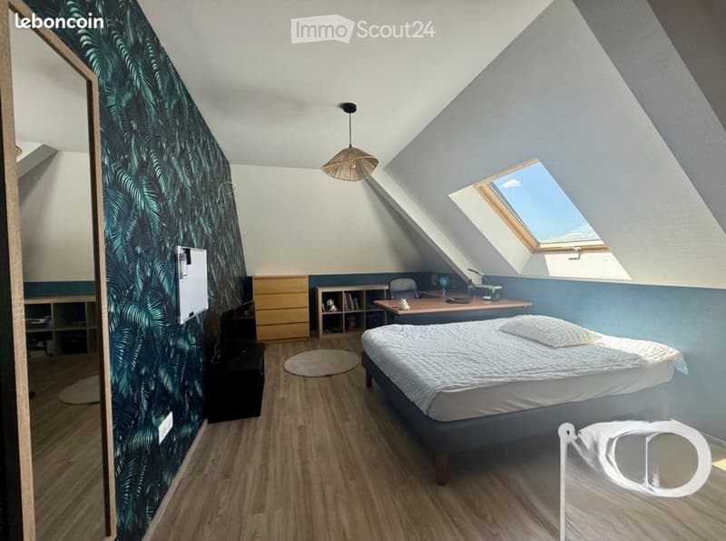 Cozy attic bedroom with wooden flooring, slanted ceilings, skylight window, bed, desk, chair, bookshelf, and decorative lamp.