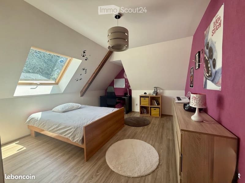 Cozy attic bedroom with wooden flooring, slanted ceilings, skylight window, bed, desk area, nightstand, and storage unit.