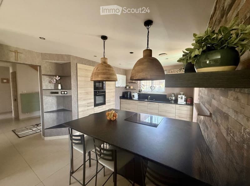 Modern kitchen with dark countertops, white cabinets, pendant lights, and a central island with chairs.